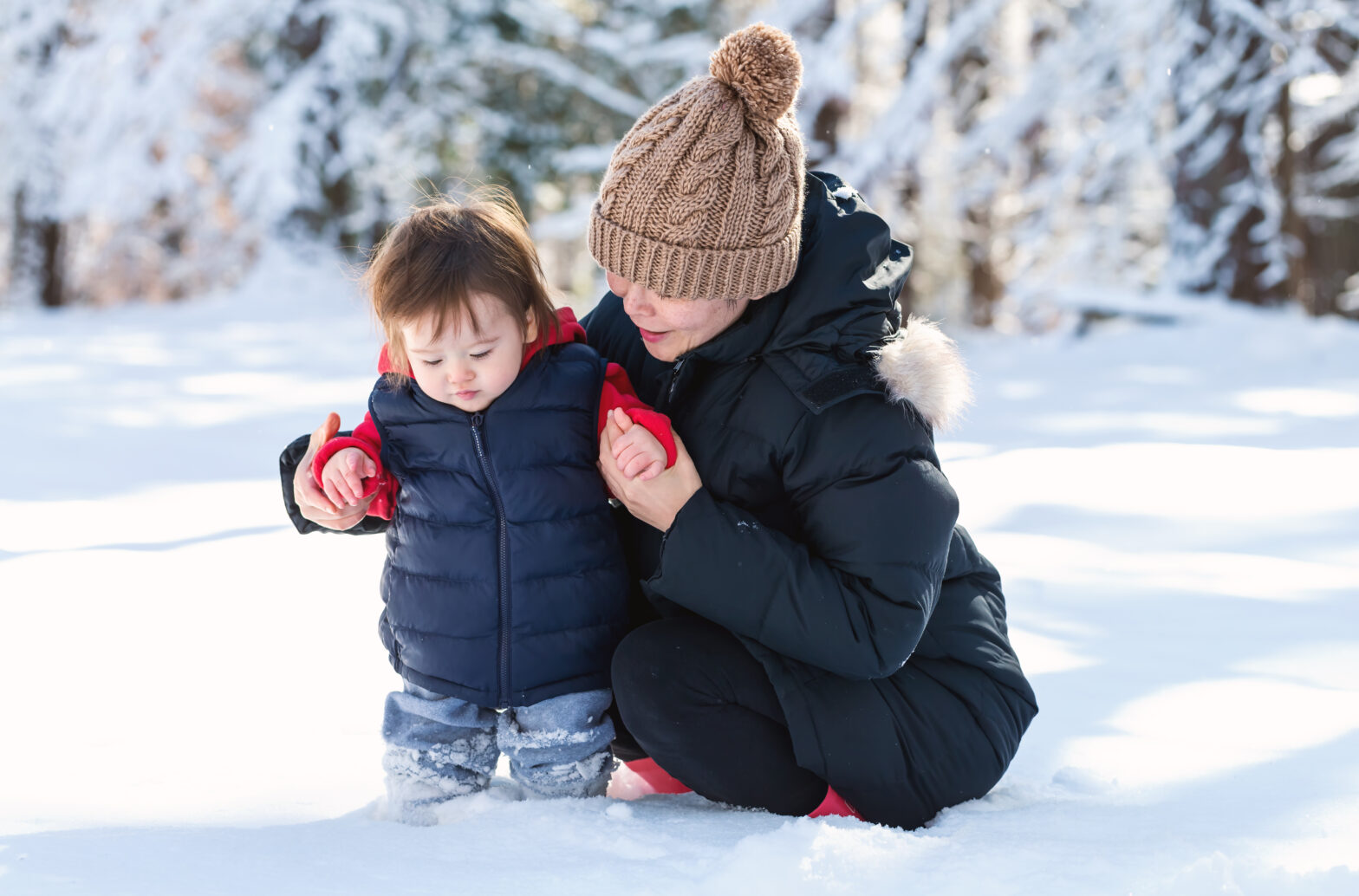 Toddler boy playing in the snow with his mother