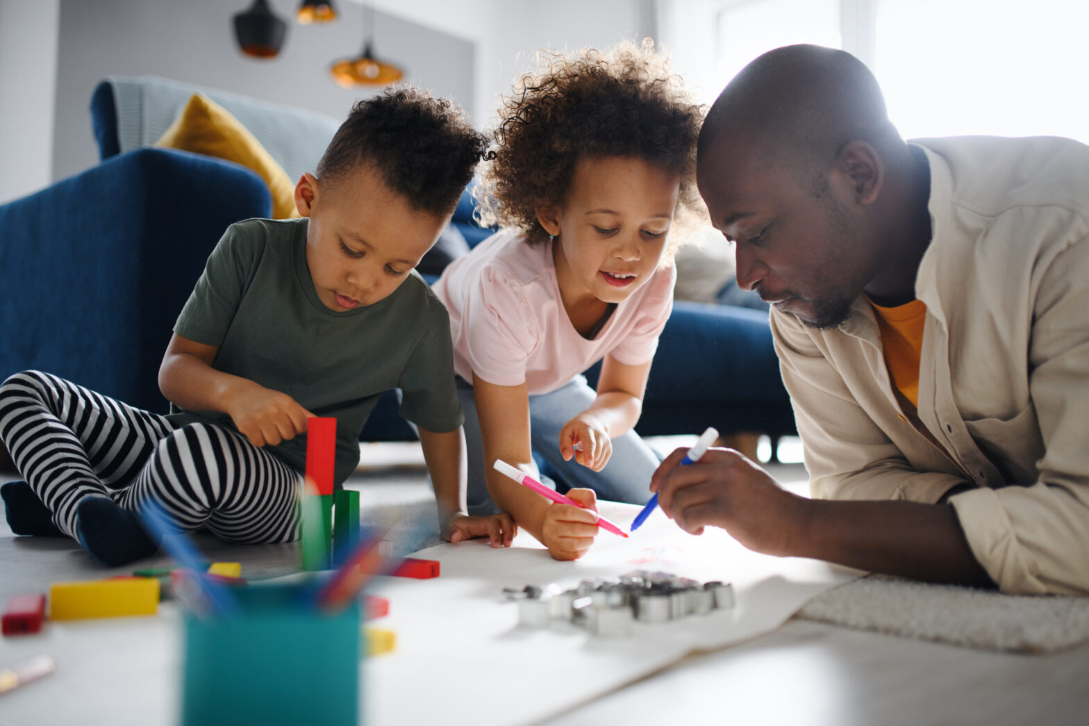 Portrait of father with two small children drawing pictures at home