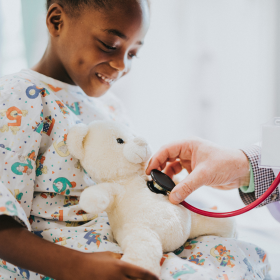 Young child in hospital gown holding stuffed teddy bear at medical appointment