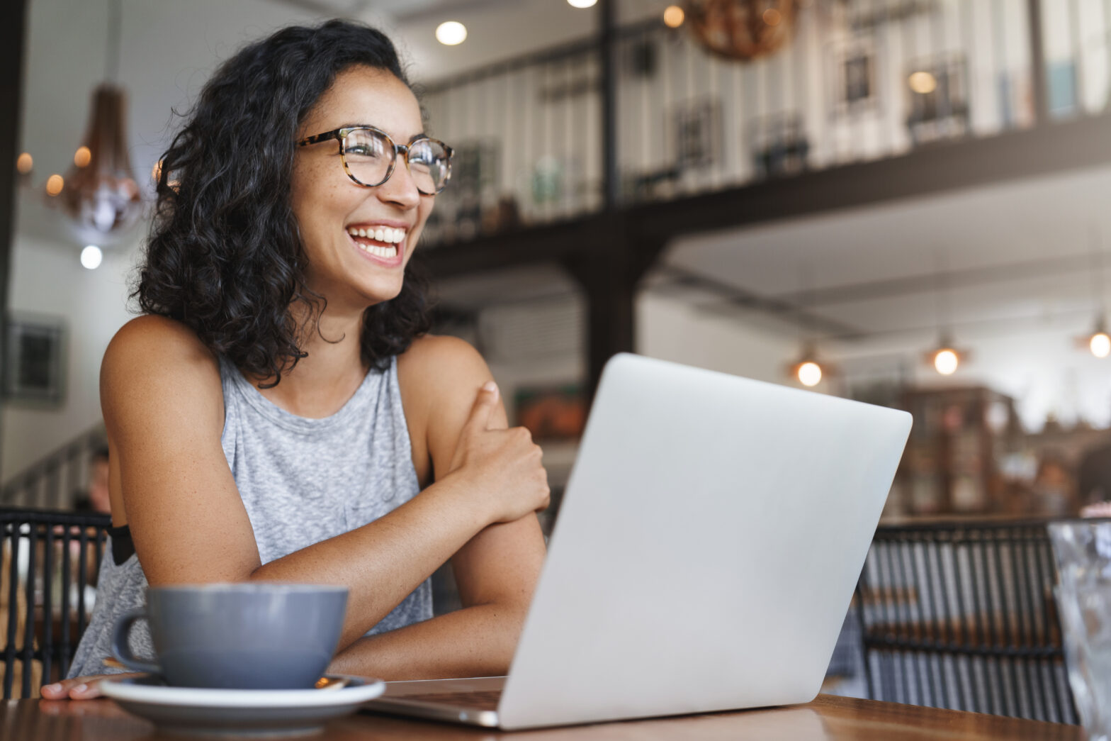 side shot of smiling woman wearing glasses with laptop and coffee mug