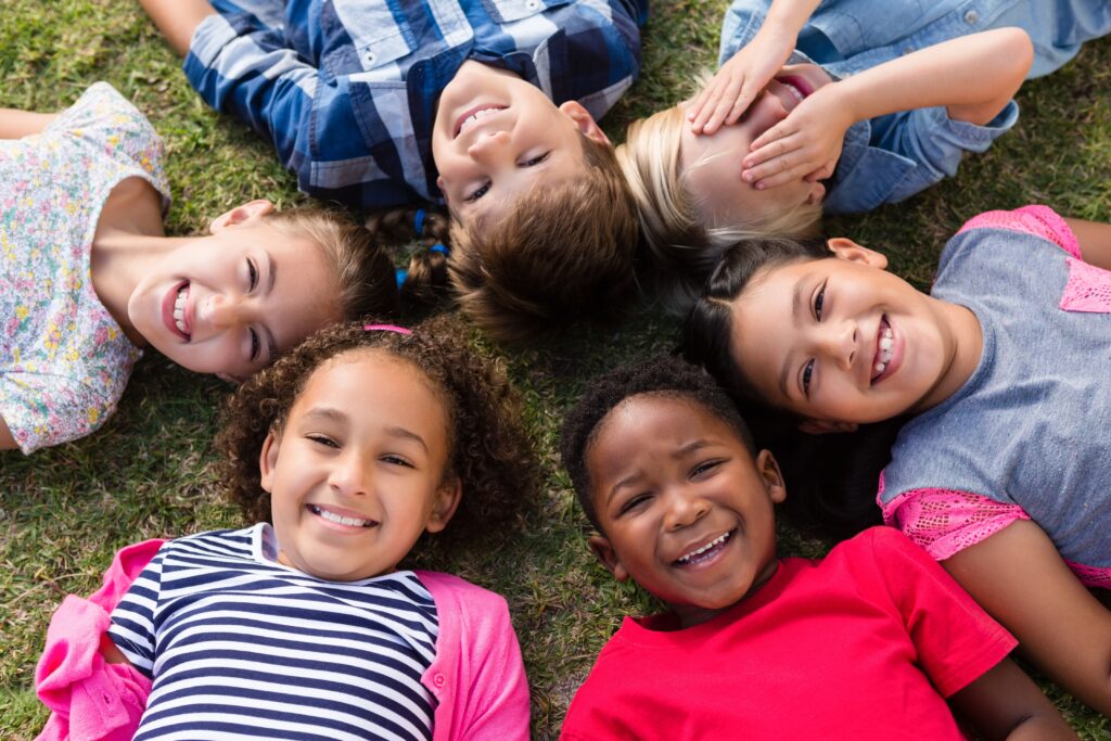 several children laying down in grass in a circle smiling