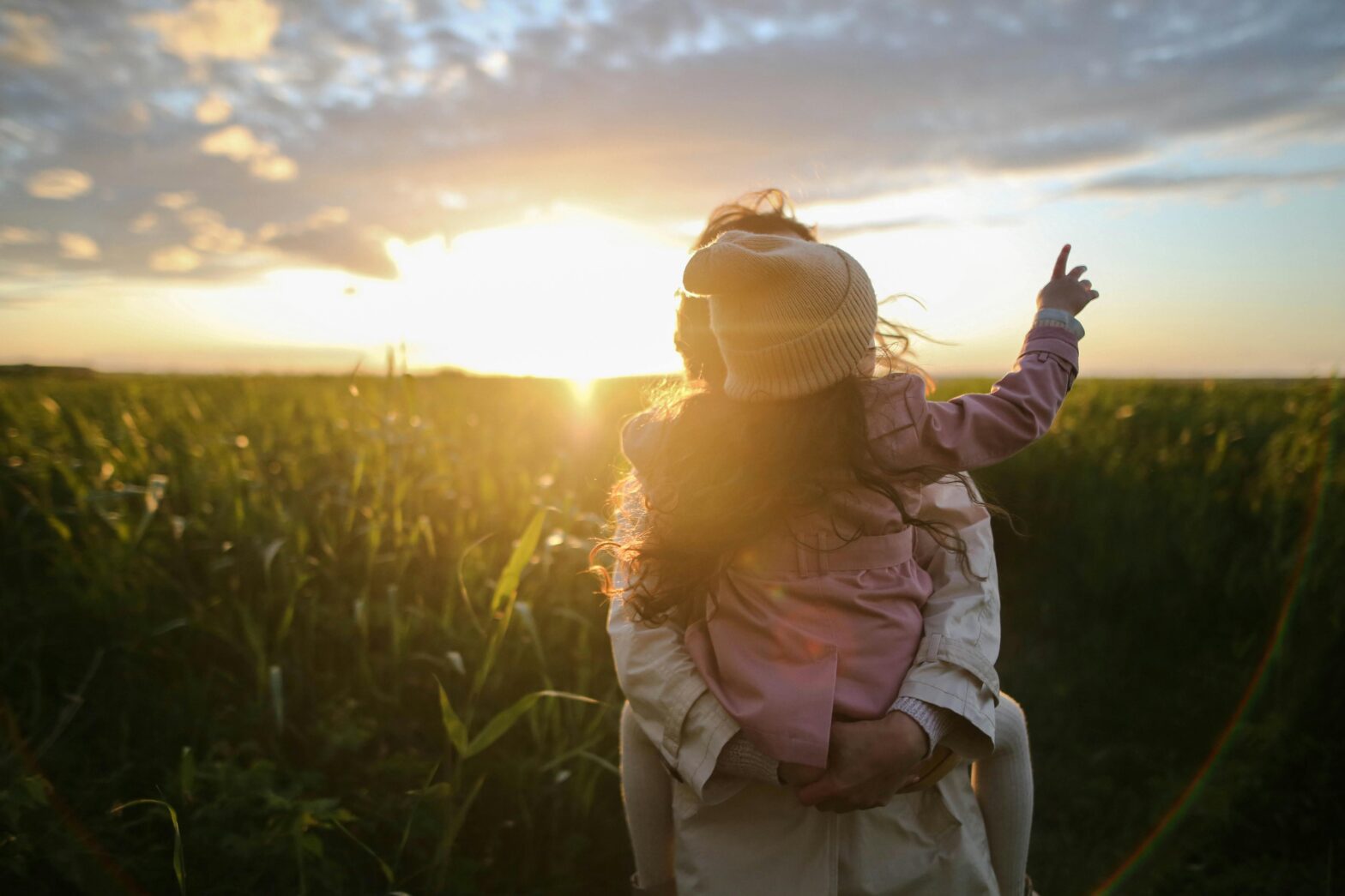 mother carrying daughter watching sunset in field